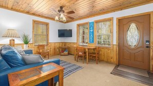 Ein gemütliches Wohnzimmer mit einem blauen Sofa, einem Holzesstisch und einem an der Wand montierten Fernseher.