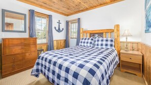 Ein Schlafzimmer mit Holzboden, einem Bett mit kariertem Bettzeug, einer Holzkommode und einem Nachttisch mit Lampe.
