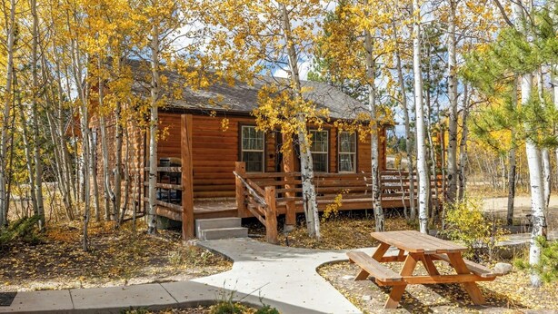 Eine Holzhütte mit Veranda, umgeben von Bäumen mit gelben Blättern.