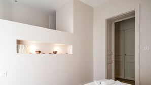 Una habitación de hotel con dos camas, una estantería empotrada con libros y objetos decorativos, y una puerta que da a un armario.