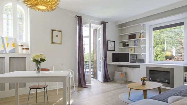 Una sala de estar moderna con un sofá blanco, una mesa de comedor con sillas, un televisor y una chimenea.