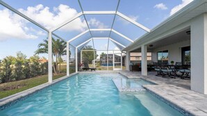 A swimming pool with a glass enclosure, outdoor seating, and a view of the surrounding landscape. - Luxury Cape Coral Retreat Pool, Hot Tub, Beautiful Outdoor Oasis & Pet Friendly (Cape Coral)