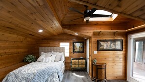 Ein Schlafzimmer in einer Holzhütte mit einem Bett, einer Kommode und einem Deckenventilator.