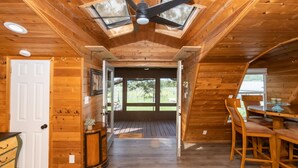 Ein Holzinterieur mit Deckenventilator, einem Esstisch mit Stühlen und Blick durch eine Tür in einen Außenbereich.