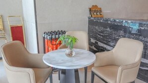 A round table with two beige chairs, a vase with a plant, and a black and white abstract painting on the wall. - Greentree Eastern Nanjing Xianlin University City Hotel (Nanjing)