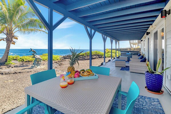 An outdoor seating area with a table set for two, overlooking a beach with a clear view of the ocean.