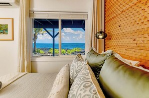 A room with a view of the ocean through a window, a bed with pillows, and a wall with a woven pattern. - Absolute Oceanfront on Ancient Lava Cliffs! Whales, dolphins, turtles! (Keaau)