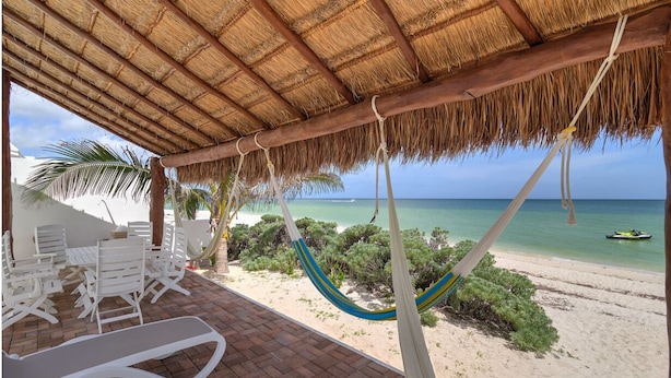 A beachside lounge with a thatched roof, white lounge chairs, and a hammock. - Casa Sara  -  Yucatan Home Rentals (Chicxulub Puerto)