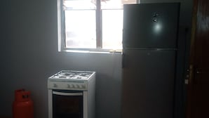 A compact kitchen with a gas stove, a refrigerator, and a window providing natural light. - JiL Service Flat (Ibadan)