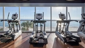 A gym with three treadmills, large windows, and a view of the beach.
