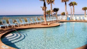 A pool area with lounge chairs and palm trees, overlooking the sea.