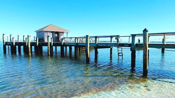 Un muelle que se adentra en aguas cristalinas con una pequeña construcción de madera al final.