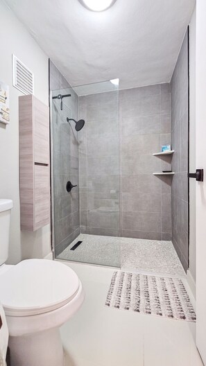 Une salle de bain moderne avec une douche à parois de verre, des toilettes et un tapis à motifs.
