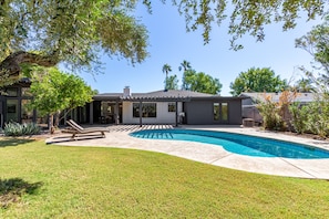 Ein modernes Haus mit Swimmingpool, überdachter Terrasse und gepflegtem Rasen.