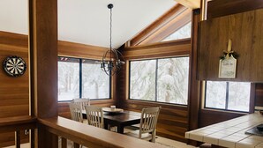 A dining area with a wooden table and chairs, a chandelier, and windows with a snowy view. - Our Lake Tahoe H💙ME<br> (Tahoe City)