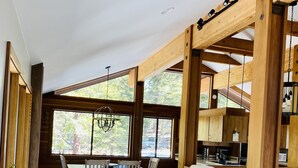 A spacious kitchen with wooden beams, a dining area with a table and chairs, and large windows offering a view of the outdoors. - Our Lake Tahoe H💙ME<br> (Tahoe City)