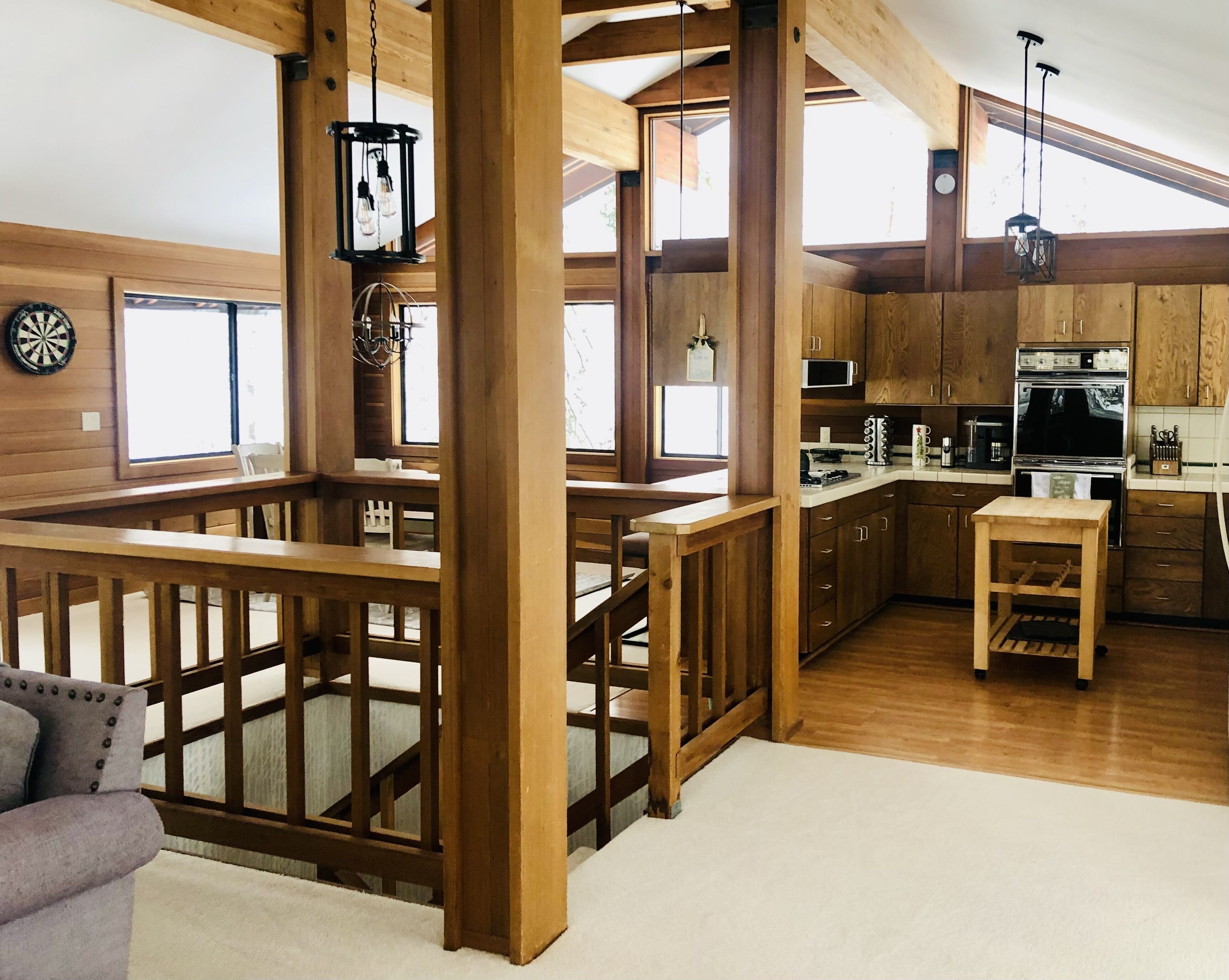 Un vaste espace de vie de style loft, doté d’un escalier en bois, d’un coin cuisine avec des appareils modernes et d’un espace repas avec un haut plafond en bois et de grandes fenêtres.