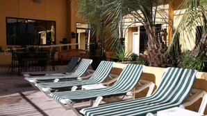 Fileira de cadeiras de lounge listradas alinhadas em um pátio de concreto, com uma palmeira e um edifício ao fundo.