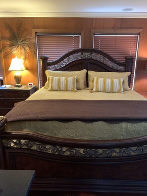 A neatly made bed with a brown headboard and decorative pillows, a bedside lamp, and a clock.