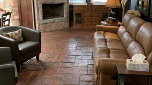 A living room with a stone fireplace, leather sofa, and a television mounted on the wall. - Beautiful home and/or garage apartment, minutes from Oaklawn Park. (Hot Springs)