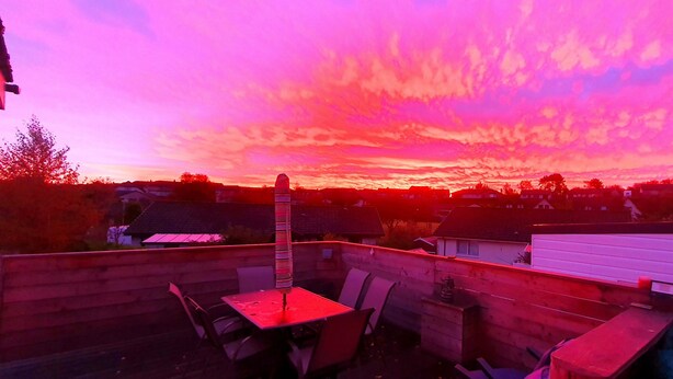 Une terrasse sur le toit, avec une table et des chaises, d’où l’on peut admirer un quartier résidentiel au coucher du soleil.
