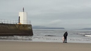 Une plage avec une grande structure en béton, qui pourrait être une digue, et une personne se tenant près de l’eau.