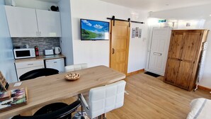 Une cuisine compacte avec des meubles blancs, un four à micro-ondes, une bouilloire et une table à manger en bois.