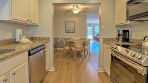 A kitchen with white cabinets, a granite countertop, a dishwasher, a stove, and a dining area with chairs and a table. - Shipyard Cottage - Private Beach & Golf! Pet Friendly! Free beach chairs,towels. (Hilton Head Island)