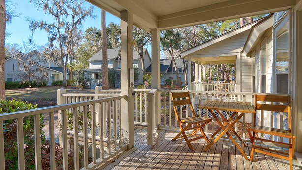 A covered porch with a wooden table and chairs, surrounded by white railings and a view of neighboring houses. - Shipyard Cottage - Private Beach & Golf! Pet Friendly! Free beach chairs,towels. (Hilton Head Island)