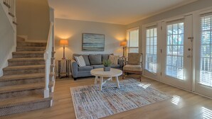 A living room with a staircase, a gray sofa, a round coffee table, and a patterned rug. - Shipyard Cottage - Private Beach & Golf! Pet Friendly! Free beach chairs,towels. (Hilton Head Island)