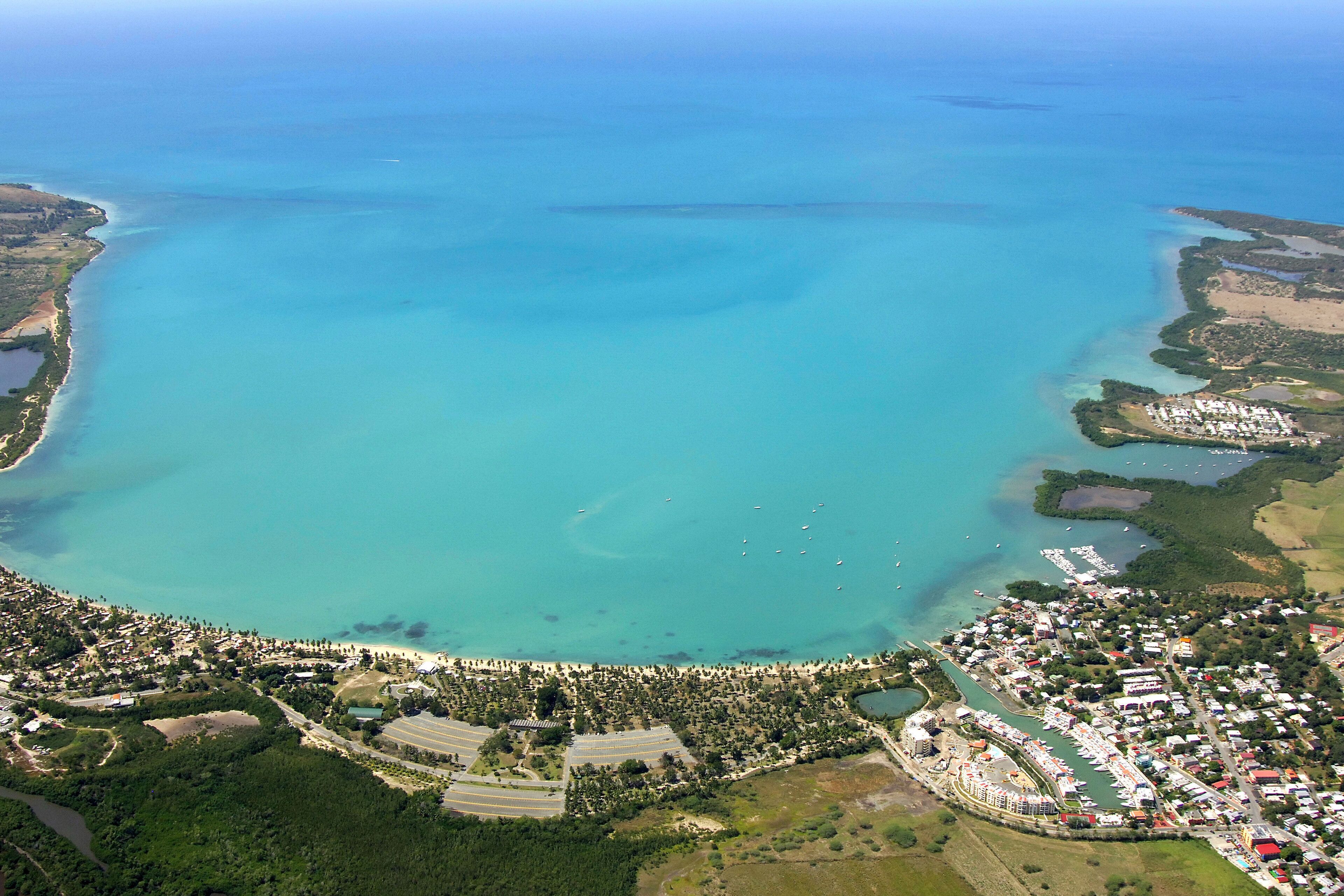 An aerial view of a coastal area with a marina, residential buildings, and a large body of water.