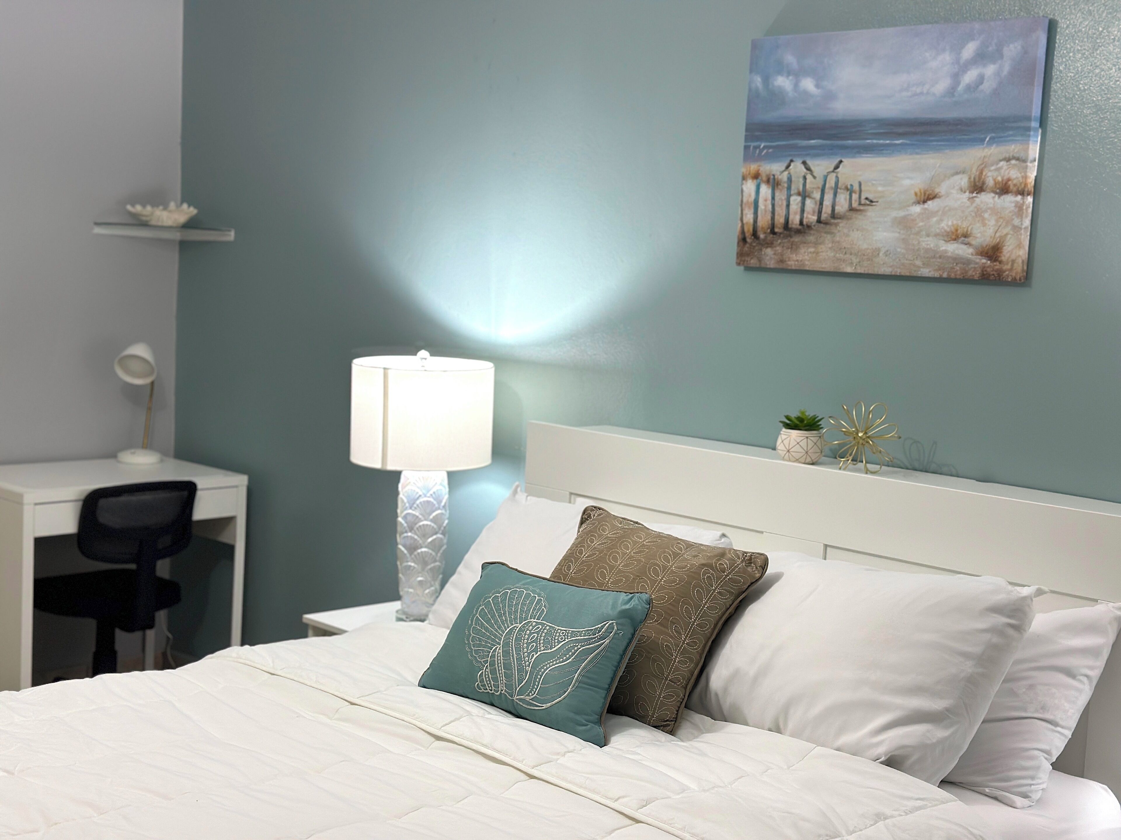 A neatly arranged bedroom with a bed, a desk, and a lamp.