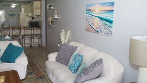 A living room with a white sofa, patterned rug, and a painting of a beach scene.
