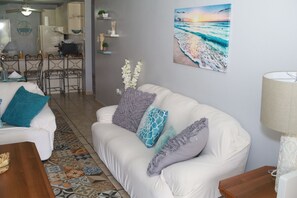 A living room with a white sofa, patterned rug, and a painting of a beach scene.