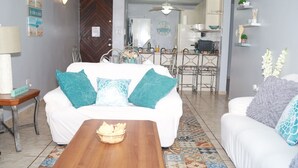 A living room with a white sofa, teal pillows, a wooden coffee table, and a patterned floor.