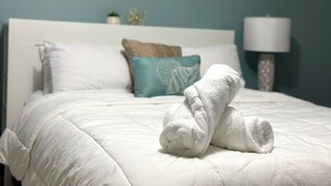 A neatly made bed with white bedding and two rolled towels placed on top.