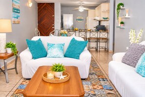 A living room with a white sofa, teal cushions, a wooden coffee table with a plant, and a patterned rug.