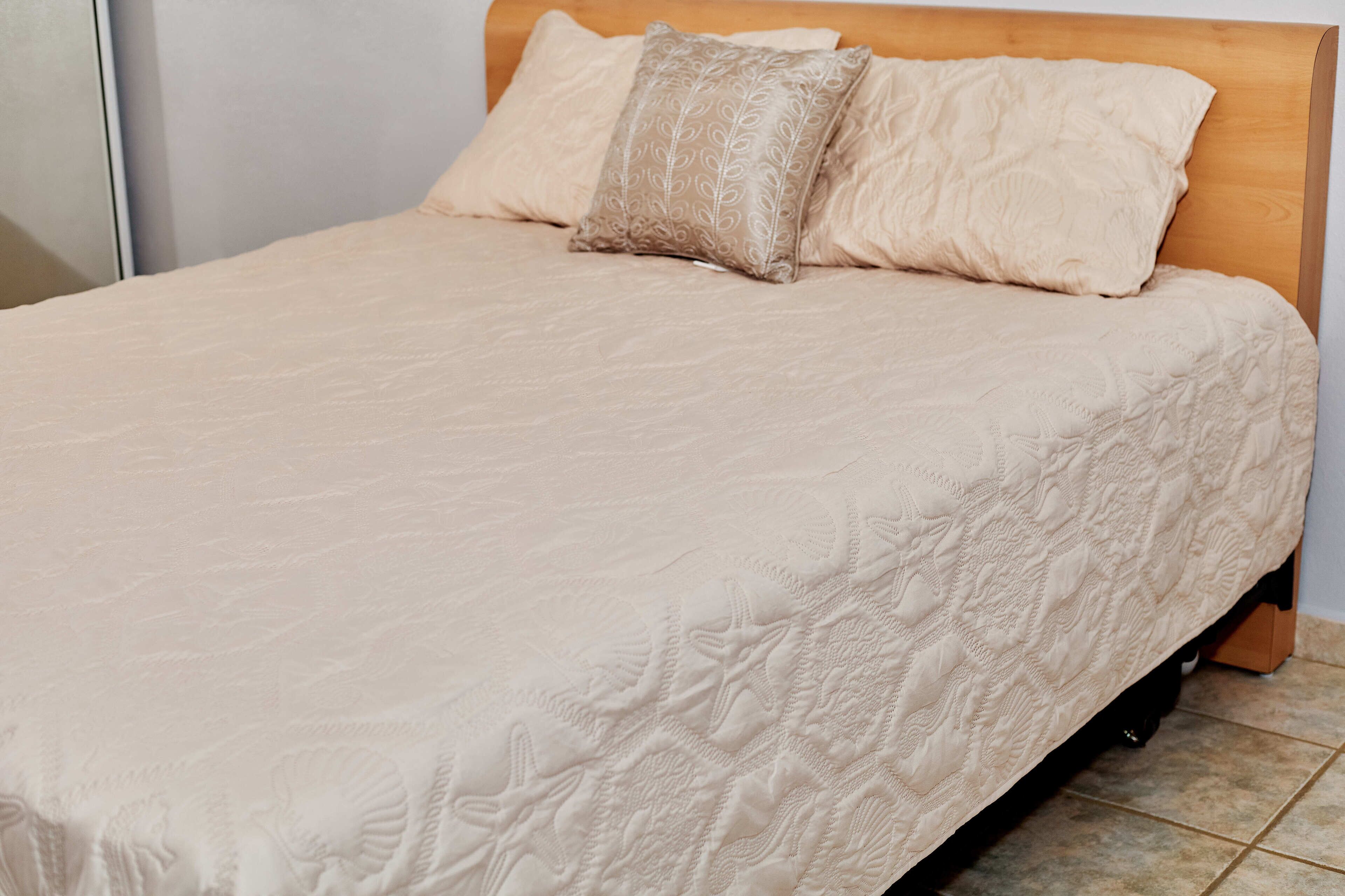 A bed with a wooden headboard, two pillows, and a textured bedspread.