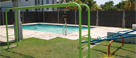 A swimming pool with a green and blue slide, surrounded by a fenced yard and a grassy area.