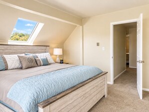 A bedroom with a sloped ceiling, a skylight, a bed with a wooden headboard, a bedside table with a lamp, and a door leading to a closet. - Lake View Casa (Fort Collins)