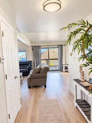 A living room with a sofa, a plant, and a view of a mountainous landscape through a window. - Lake View Casa (Fort Collins)