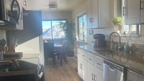 A modern kitchen with stainless steel appliances, white cabinets, and a large window providing a view of the outdoors. - Lake View Casa (Fort Collins)