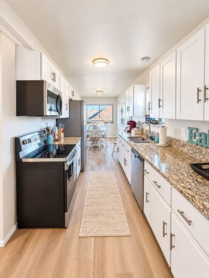 A modern kitchen with white cabinetry, stainless steel appliances, and a granite countertop. - Lake View Casa (Fort Collins)