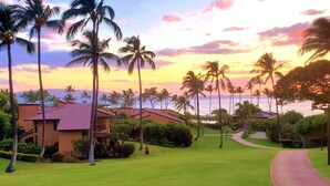 A resort with a view of the ocean at sunset, featuring palm trees and a pathway leading to a building. - Wailea Ekahi 10C - Just steps away from Main Pool & Beach!  - Family Managed (Kihei)