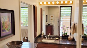 A bathroom with a vanity, sink, and mirror. There is a framed picture on the wall, a towel rack, and a window with blinds.