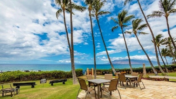 A patio with a table and chairs, palm trees, and a view of the ocean. - Wailea Ekahi 10C - Just steps away from Main Pool & Beach!  - Family Managed (Kihei)