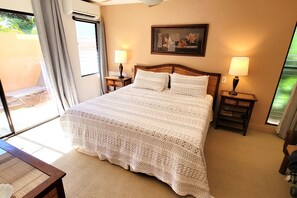 A hotel room with a large bed, two bedside lamps, a wooden headboard, a framed picture on the wall, and a view through the window.