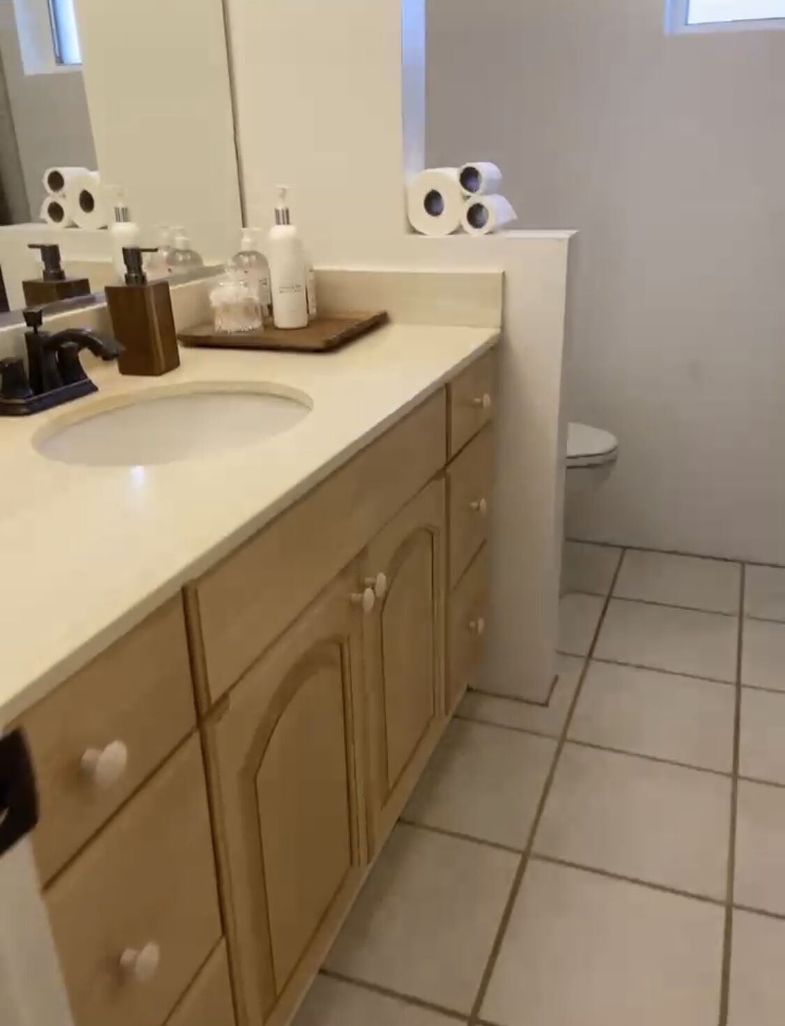 A modern bathroom with a beige countertop, a sink, and a toilet. There are toiletries on the counter and a mirror above the sink.