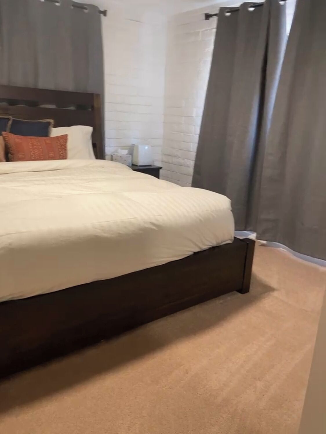 A neatly made bed with a dark wooden frame, a white headboard, and a beige carpet.