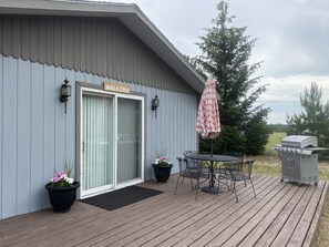 Un bâtiment sur lequel on peut lire l’inscription « BIENVENUE », une terrasse couverte avec une table et des chaises, et un barbecue.